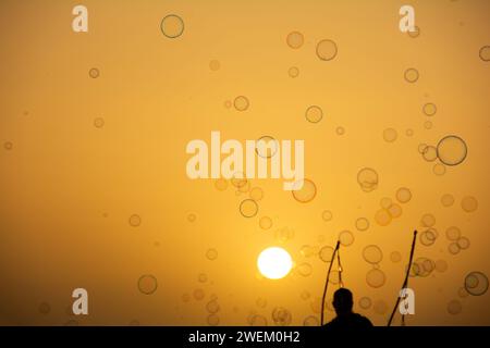 Un homme en silhouette fait beaucoup de bulles de savon avec un bâton de bulles de savon, elles flottent dans le ciel orange au coucher du soleil Banque D'Images
