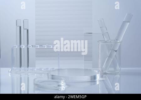 Science et formation médicale avec podium rond transparent, verrerie de laboratoire remplie de liquide incolore et feuilles acryliques nervurées décorées sur fond blanc Banque D'Images