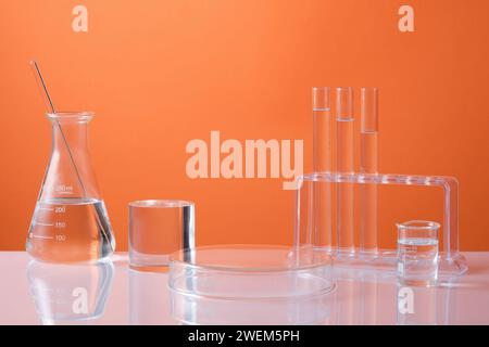 Vue avant de l'équipement de laboratoire - flacon erlenmeyer, tubes à essai et bécher rempli de liquide incolore et podium de bouteille pour la présentation du produit sur o Banque D'Images