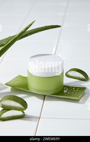 Un pot de crème non étiqueté placé sur des tranches fraîches d'aloe vera sur fond blanc. Cosmétique, maquette de produit de beauté avec ingrédient de l'aloe vera - hydratant Banque D'Images