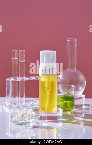 Vue de face de la bouteille jaune sans étiquette sur podium transparent et verrerie de laboratoire contenant du liquide décoré sur fond rose. Maquette pour produit cosmétique Banque D'Images