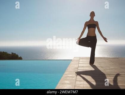 Young woman practicing yoga par une piscine avec l'océan dans l'arrière-plan Banque D'Images