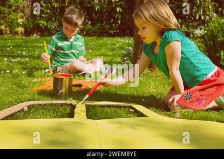 Garçon et fille des découpes de carton de peinture dans le jardin Banque D'Images