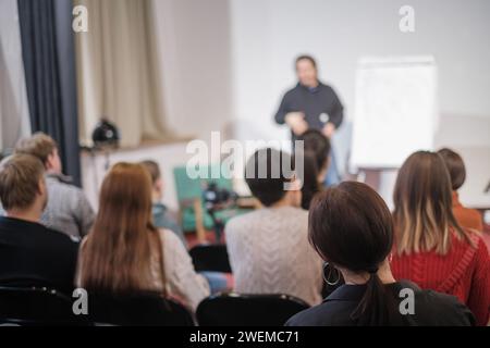 Vue arrière d'un public écoutant attentivement un haut-parleur flou lors d'une session de formation professionnelle. Banque D'Images