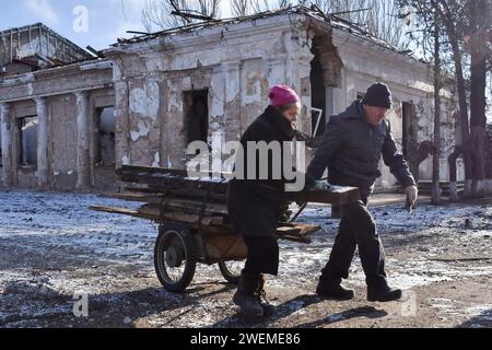 Orikhiv, Ukraine. 23 janvier 2024. Un couple âgé transportant les planches de bois sur la brouette près du bâtiment municipal historique qui a été lourdement endommagé par les bombardements russes à Orikhiv. Orikhiv est une petite ville près de Zaporizhjhia, qui sert de dernier pilier de résistance pour les soldats de l'armée ukrainienne dans le sud, alors que les forces armées russes continuent d'avancer vers la Robotyne libérée. Abritant environ 700 personnes, les citoyens d'Orikhiv risquent leur vie en subissant les attaques quotidiennes de bombes aériennes et d'artillerie alors qu'ils luttent pour survivre. Crédit : SOPA Images Limited/Alamy Live News Banque D'Images