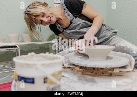 Femme est assise à la roue de poterie tout en jetant des pots dans le home studio Banque D'Images