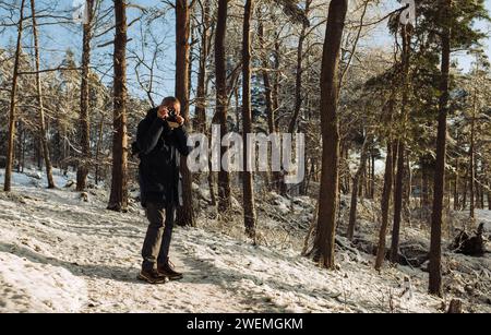 homme retraité marchant dans la neige dans la forêt en prenant des photos Banque D'Images