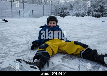 garçon allongé sur la glace patinant dehors Banque D'Images