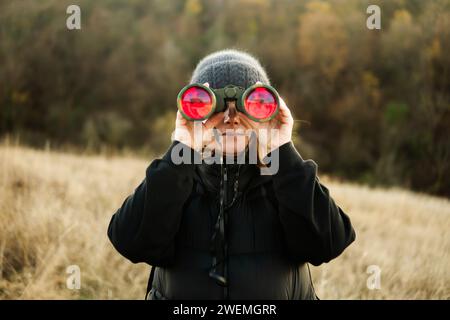 Femme regardant à travers des jumelles à une ferme Banque D'Images