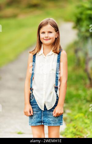 Portrait en plein air d'une jolie petite fille portant une chemise blanche et une jupe en denim avec bretelles Banque D'Images