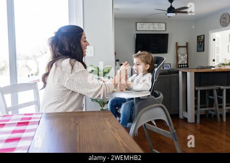 Mère nourrissant sa petite fille déjeuner assis dans une chaise haute Banque D'Images