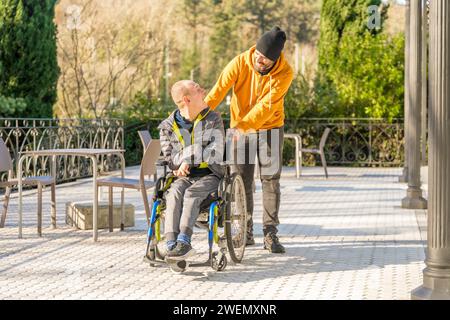 Soignant poussant le fauteuil roulant d'un homme handicapé souriant dans un parc urbain Banque D'Images