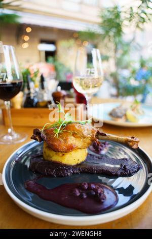 Cuisse de canard rôtie sur purée de pommes de terre avec oignon, crème de chou violet et jus de myrtilles sur une table extérieure Banque D'Images