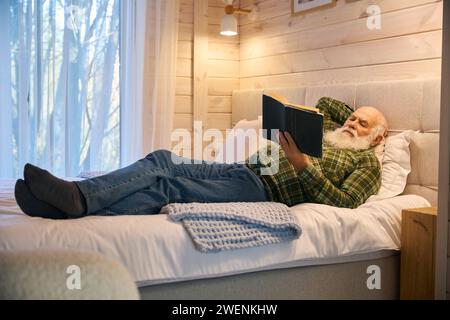 Le vieil homme s'allongea avec un livre sur un lit confortable Banque D'Images