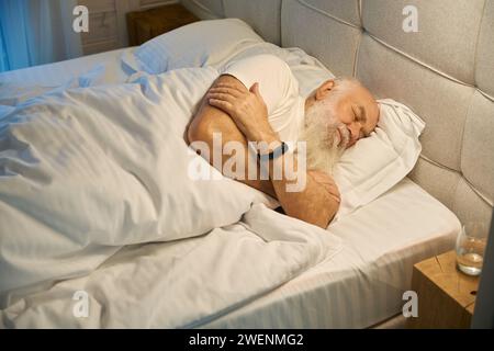 Un homme âgé dort sur le côté dans un lit confortable Banque D'Images