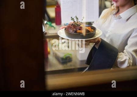 La jeune serveuse sert de la viande garnie d'une branche de thym Banque D'Images