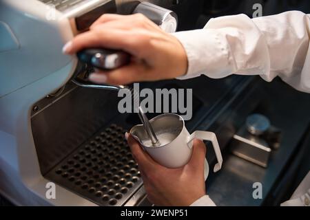 Barista en blouse blanche fait de la mousse de lait dans la machine à café Banque D'Images