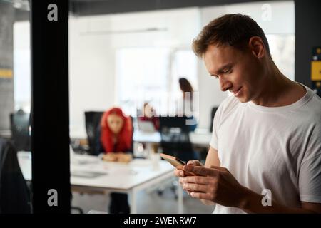 Gros plan beau jeune homme jouant à des jeux sur smartphone au lieu de travailler Banque D'Images