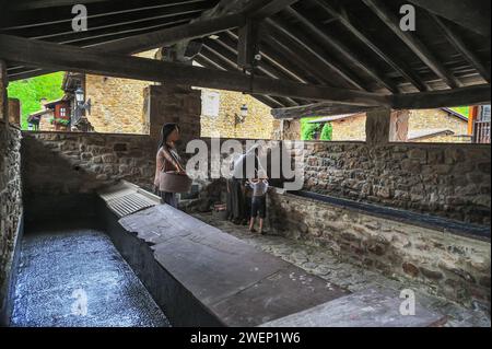 Les résidents participent à la vie quotidienne dans la buanderie commune, un témoignage des coutumes locales à Barcena Mayor, Cantabrie, Espagne. Banque D'Images