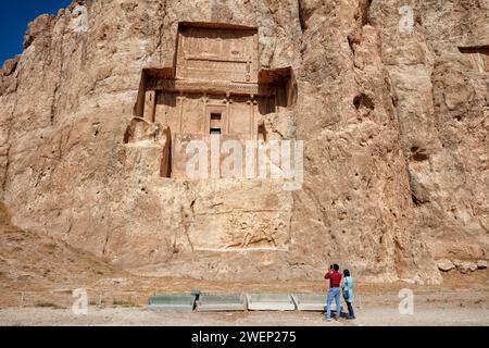 Les touristes regardent le tombeau taillé dans la roche de Darius II, roi perse (423-405 av. J.-C.) de la dynastie achéménide. Nécropole Naqsh-e Rostam près de Persépolis, Iran. Banque D'Images