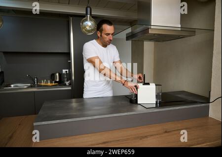 Beau jeune homme adulte des années 40, préparant du café expresso pour le petit déjeuner le matin, insérant une capsule avec arabica moulu à l'intérieur d'une capsule de café Banque D'Images