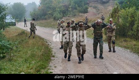 Un groupe de soldats d'élite conduit les captifs dans un camp militaire, mettant en évidence une atmosphère tendue de détention et d'opérations de sécurité Banque D'Images