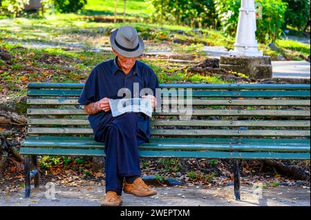 Homme senior lisant le journal dans le banc du parc, Santa Clara, Cuba Banque D'Images