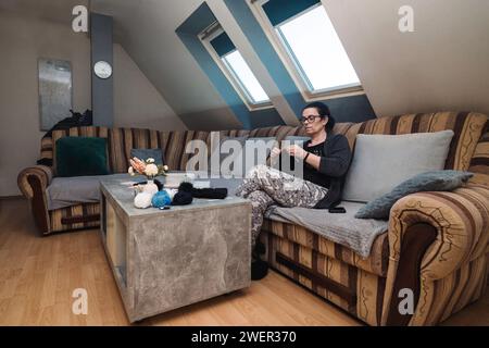 Une femme âgée assise dans son salon et tricotant avec de la laine Banque D'Images