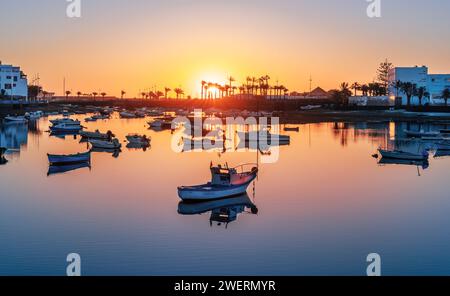 Lever de soleil Lanzarote sur Arrecife avec un bateau solitaire sur des eaux calmes. La côte de la capitale créant une scène tranquille sur le lac Charco de San Gines. Banque D'Images