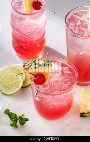 Singapore Sling cocktails dans une variété de verres garnis d'ananas et de cerise cocktail Banque D'Images