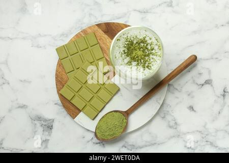 Morceaux de savoureuse barre de chocolat matcha, boisson et poudre sur table en marbre blanc, vue de dessus Banque D'Images