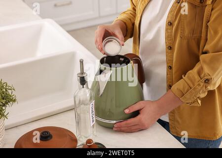 Femme ajoutant du bicarbonate de soude dans une bouilloire électrique dans la cuisine, closeup Banque D'Images