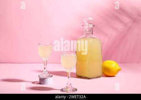 Verres et bouteille de savoureux Limoncello sur fond rose Banque D'Images