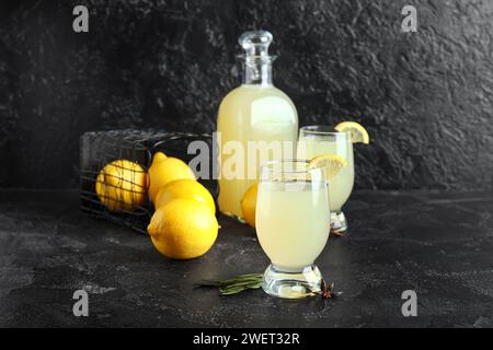 Verres et bouteille de savoureux Limoncello sur fond noir Banque D'Images