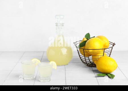 Plans de Limoncello savoureux et panier avec des citrons sur fond clair Banque D'Images