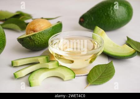 Avocats frais, feuilles et bol en verre avec de l'huile essentielle sur fond blanc Banque D'Images