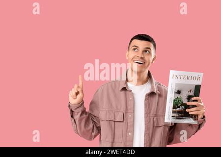 Jeune homme avec magazine pointant vers quelque chose sur fond rose Banque D'Images