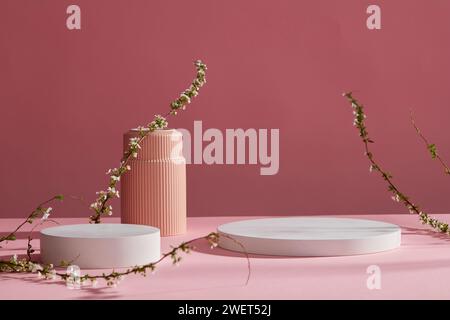 Vue de face de deux podiums vides blancs et branches de fleurs sur fond rose. Socle pour des maquettes de produit cosmétique et d'emballage présentant une présentation Banque D'Images