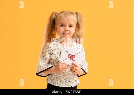 Mignonne petite fille tenant enveloppe avec des coeurs sur fond jaune. Fête de la Saint-Valentin Banque D'Images