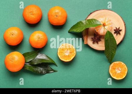 Planche de bois avec de savoureuses mandarines, des feuilles et des épices sur fond vert Banque D'Images