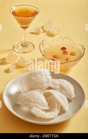 Gros plan d'un nid d'oiseau sur des plats ronds blancs, bol et tasse en verre de soupe jujube blanc et cordyceps, sucre de roche sur fond beige. Nourriture et herbe Banque D'Images