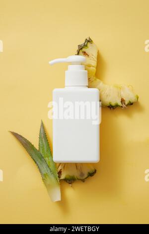 Maquette de lotion pour le corps, crème solaire ou récipient de shampooing avec distributeur de pompe. Cosmétique d'extrait d'ananas. Tranches d'ananas et feuilles sur backgroun jaune Banque D'Images