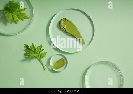 Texture crème verte sur podiums transparents, feuilles d'absinthe fraîches décorées sur fond vert. Photo publicitaire pour cosmétique d'extrait naturel - W Banque D'Images