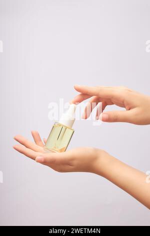 Maquette de bouteille en verre avec bouchon compte-gouttes sur la main de la femme, contenant essence jaune clair avec produit cosmétique, sérum sur fond clair. Concept de Banque D'Images