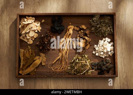 Vue de dessus des herbes chinoises traditionnelles placées sur un plateau en bois sombre, sur fond de table en bois. Scène pour la publicité de médecine, la photographie traditiona Banque D'Images