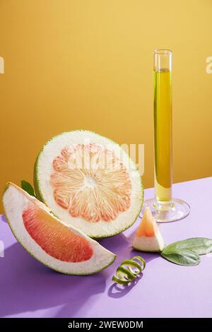 Vue de face de tranches de pomelo rose frais, feuilles vertes et tube à essai contenant l'essence sur fond jaune. Scène pour la publicité cosmétique extraite Banque D'Images