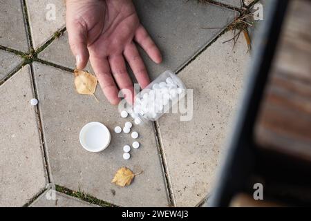 Pilules tombant des mains au sol, concept sur le thème d'une forte détérioration de la santé dans la rue Banque D'Images