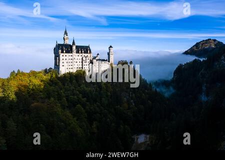 Le château Neuschwanstein, vu du pont Marienbrücke au lever du soleil en automne, se levant du brouillard. Banque D'Images