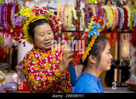 (240127) -- QUANZHOU, 27 janv. 2024 (Xinhua) -- Un villageois épingle un couvre-chef fleuri pour un touriste au village de Xunpu de la ville de Quanzhou, dans la province du Fujian du sud-est de la Chine, le 26 janvier 2024. Les coiffures fleuries Xunpu, surnommées « jardins aériens », ont été une signature des « coutumes des femmes Xunpu » inscrites au patrimoine national immatériel en 2008. Ils ont attiré des millions d'yeux dans le cybermonde au début de 2023, suivi par un boom touristique durable dans le village, où les visiteurs peuvent littéralement y tenir la tête. La prise de photos, la restauration et d'autres services d'accueil ont diversifié la source de In Banque D'Images