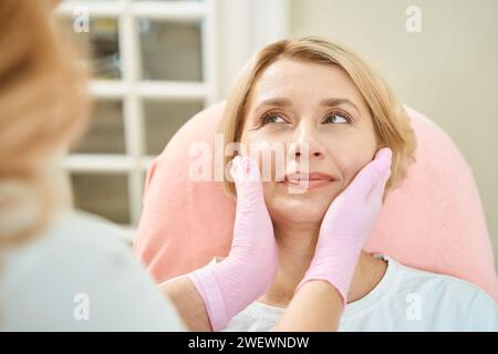 Mains d'esthéticienne partielle examinant le visage de la femme regardant cosmétologue Banque D'Images